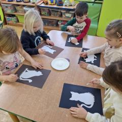 Dzieci siedzą przy stoliku i robią pracę plastyczną z okazji dnia kota