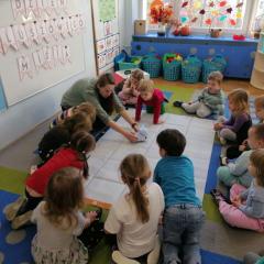 Nauczycielka ustawia robota edukacyjnego na macie do kodowania, dzieci obserwują jego trasę