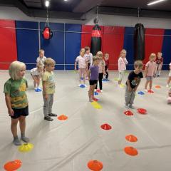 Dzieci podczas ćwiczeń, na podłodze rozłożone są kolorowe znaczniki sportowe 