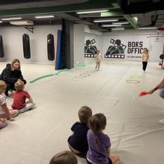   Dzieci podczas drużynowej zabawy ruchowej omijają krążki, skaczą obunóż